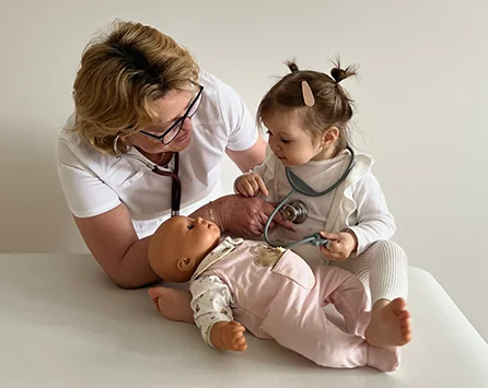 MUDr. Marta Čelková vyšetruje bábätko, malé dievčatko jej pomáha hračkárskym stetoskopom